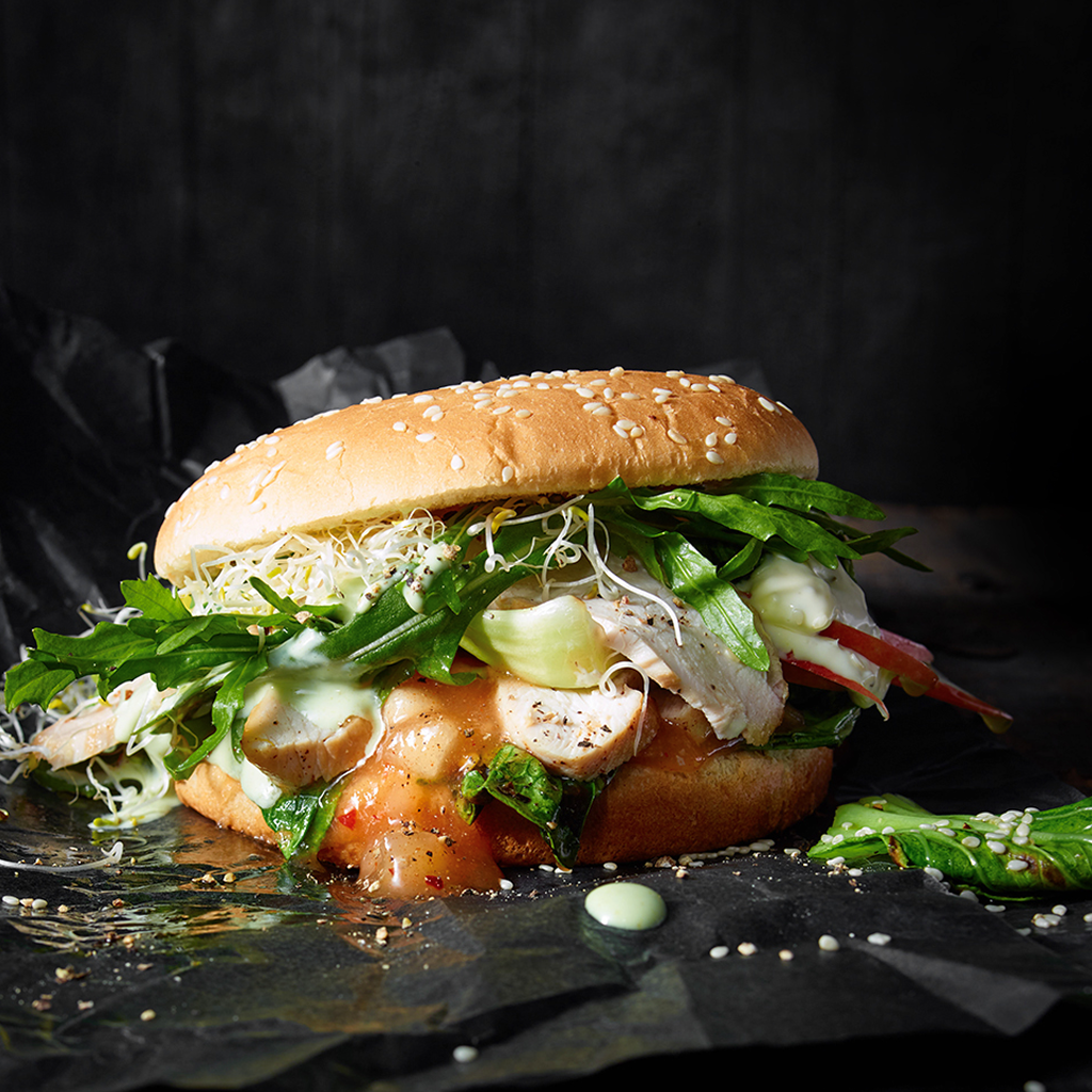 Frisch zubereiteter Chicken Burger Deluxe mit saftigem Hähnchenpatty, knackigem Salat, frischen Toppings und cremiger Sauce in einem goldbraunen Burger Bun serviert.